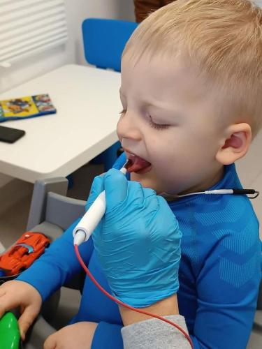 Chłopiec uczestniczy w elektrostymulacji mięśni języka podczas terapii logopedycznej wspierającej funkcje oralne i komunikacyjne. 