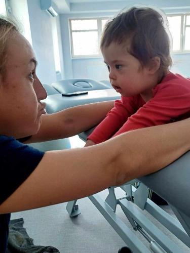 Fizjoterapeutka prowadzi ćwiczenia wspierające rozwój kontroli głowy i tułowia u małego dziecka podczas rehabilitacji funkcjonalnej. 