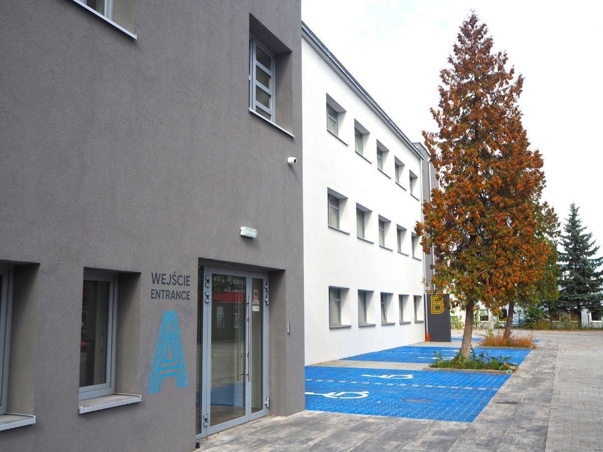 Wejście do budynku Centrum Grawitacja z oznaczeniem strefy oraz miejscami parkingowymi dla osób z niepełnosprawnościami. 
