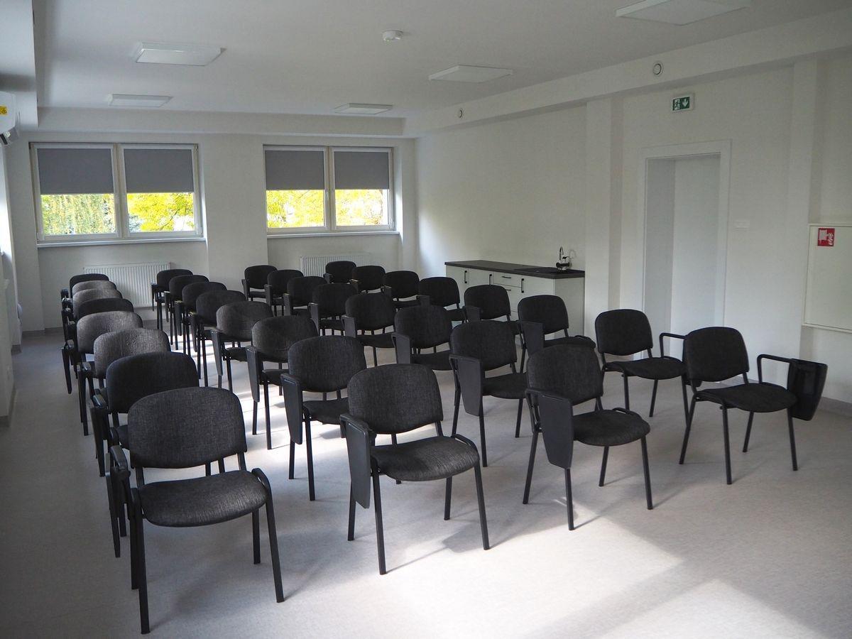 Przestronna sala szkoleniowa z rzędami krzeseł, przygotowana do organizacji konferencji, warsztatów i spotkań edukacyjnych. 